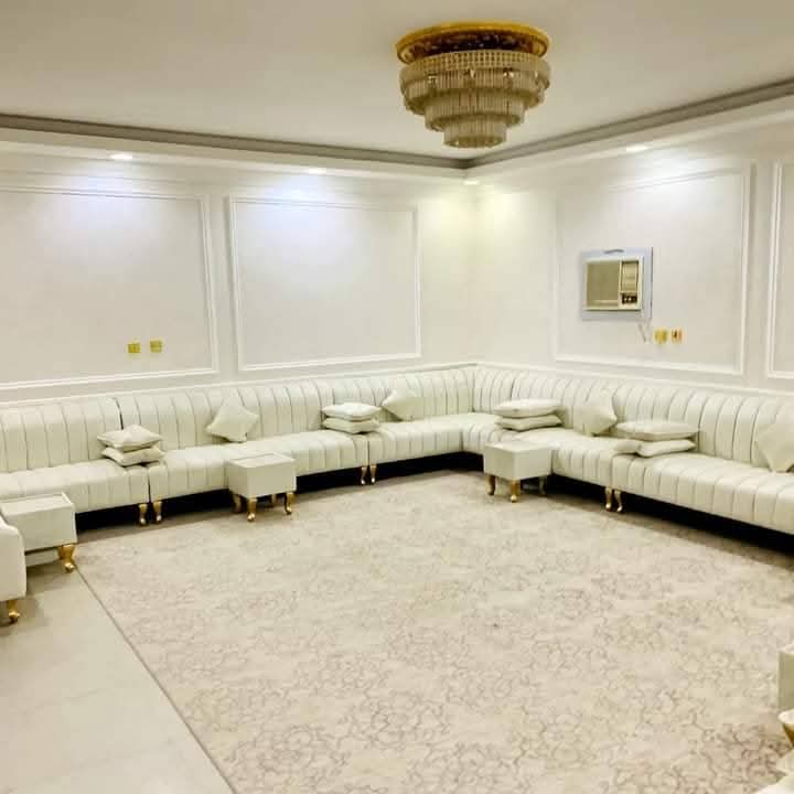 White channel-tufted sectional with gold legs beneath a crystal chandelier